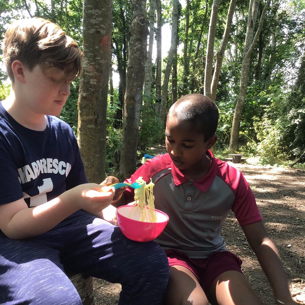 Boys eating noodles they've cooked outside