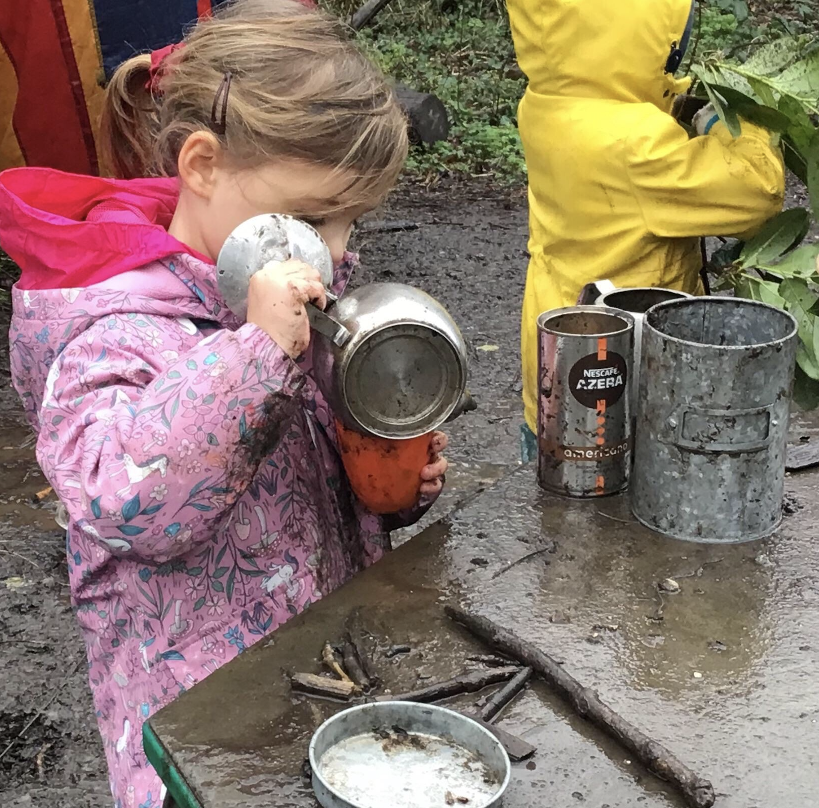 A girl making tea in the mud kitchen